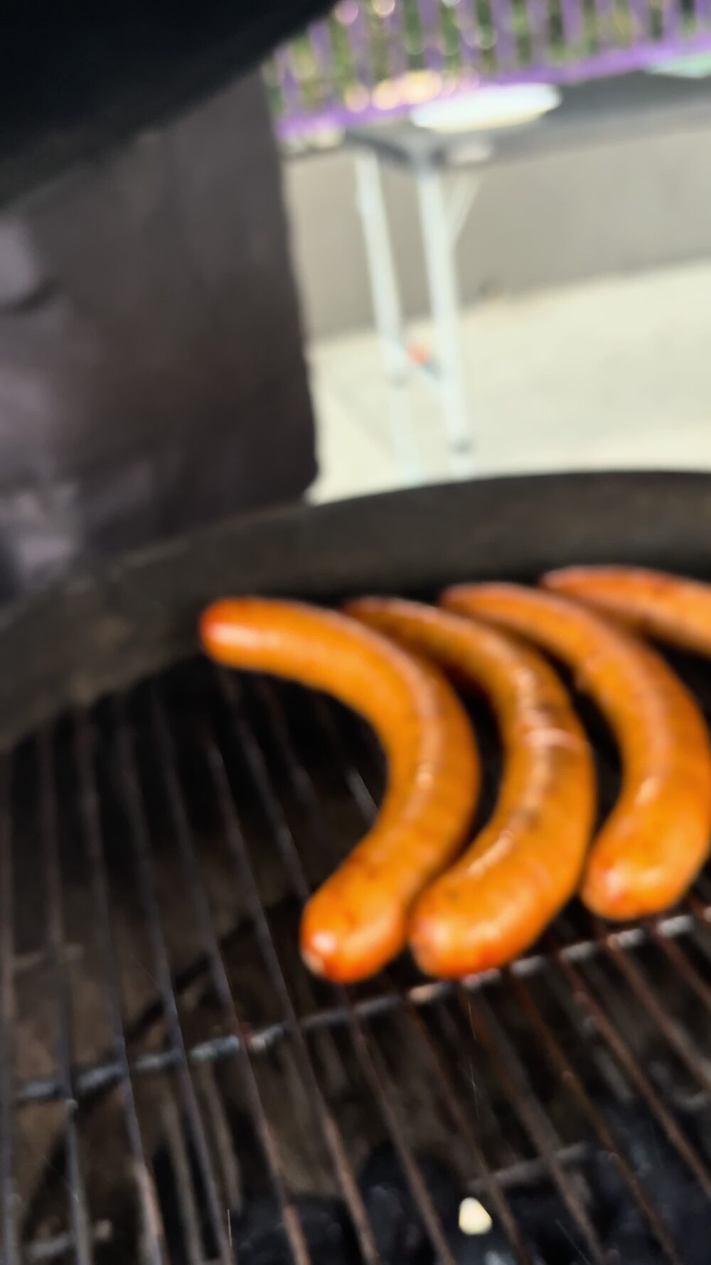 Three sausages browning on the kettle grill
