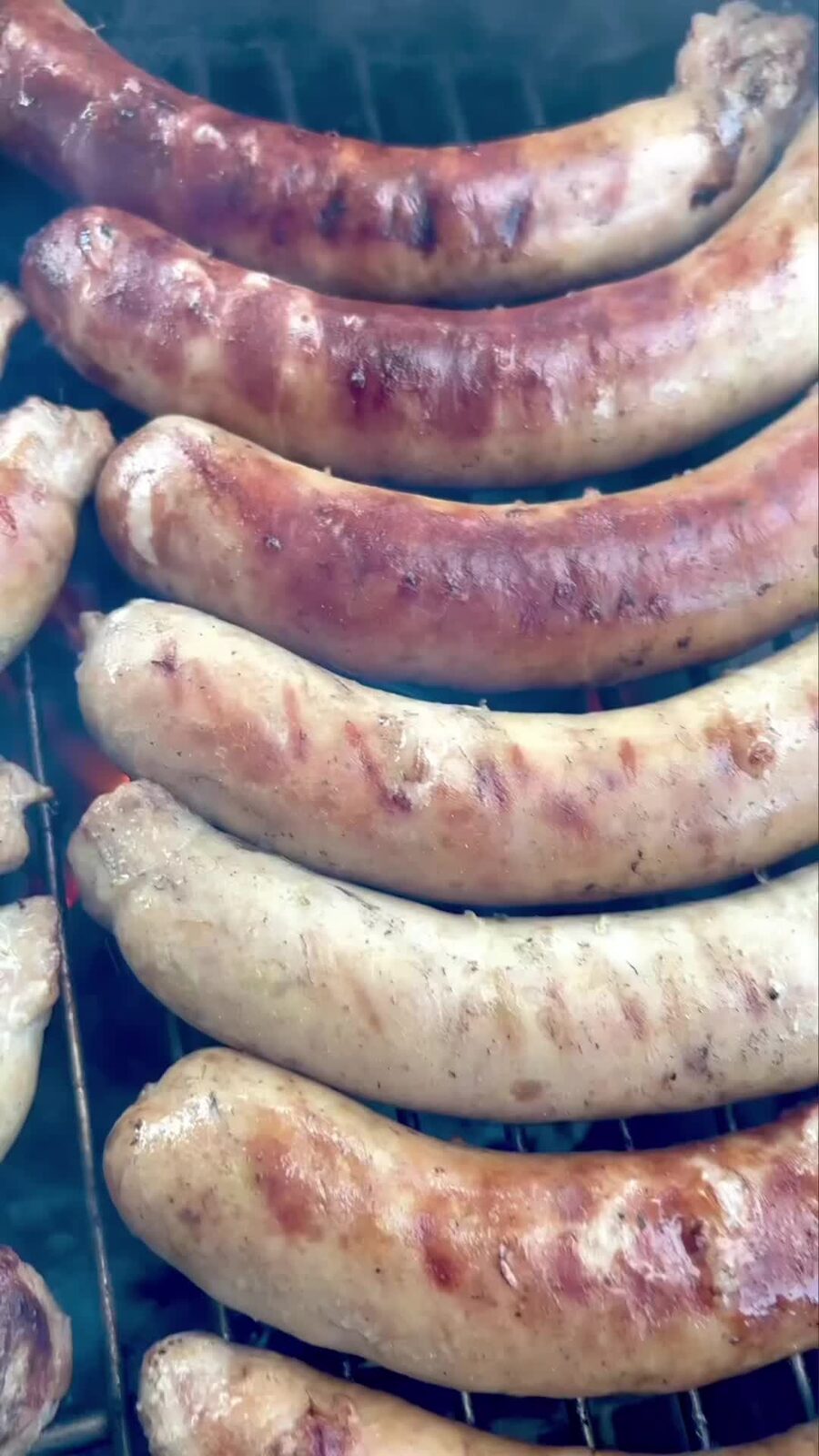 Homemade sausages browning in rows on the charcoal grill
